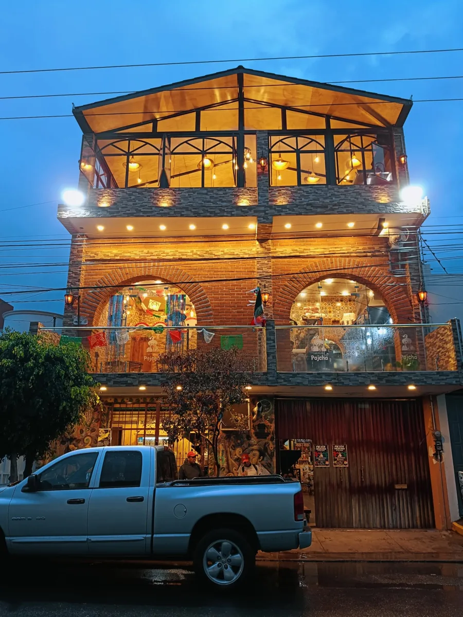 Fachada de Café Pajchá de noche: edificio de ladrillo de tres pisos con arcos iluminados